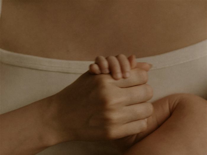 A mother's hand holding her newborn's tiny hand