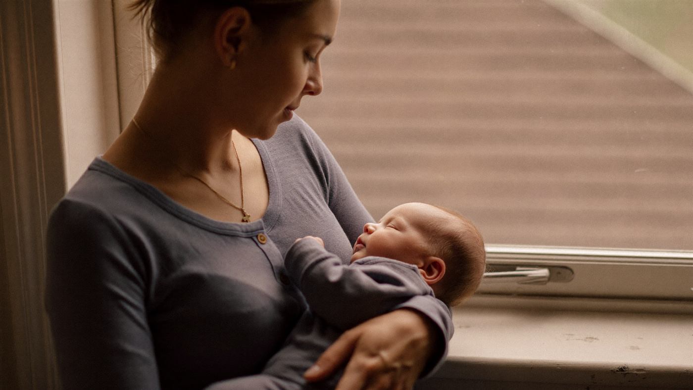 A mother gently holding her newborn by a sunlit window