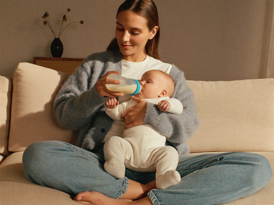 A mother bottle-feeding her baby on the sofa