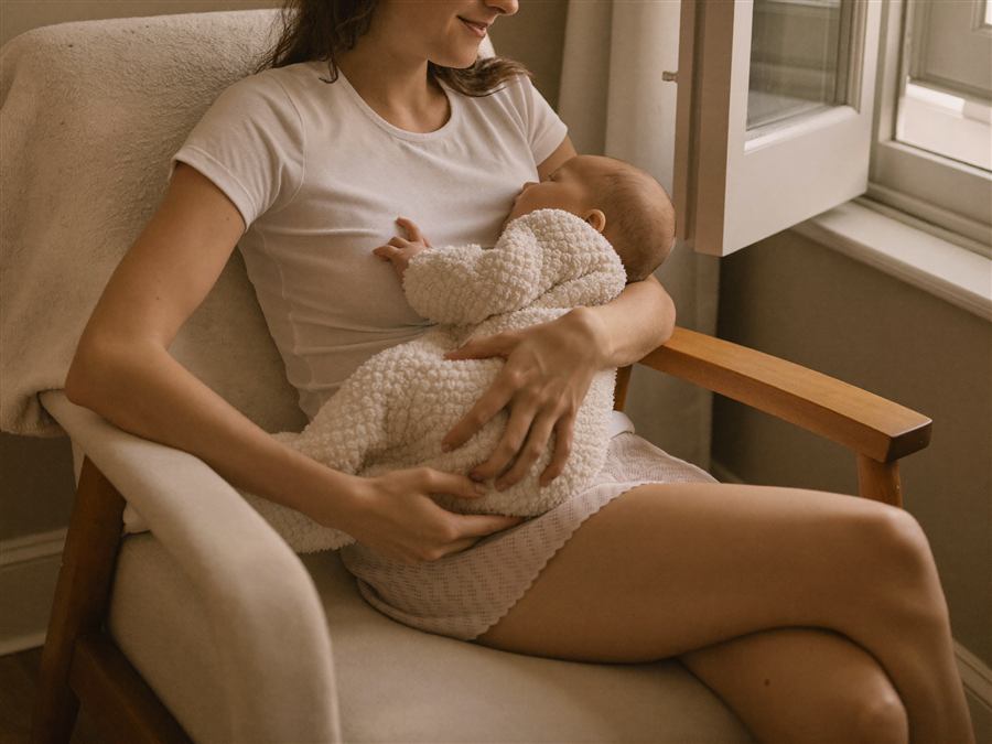 A mother nursing her baby in a cozy armchair by the window