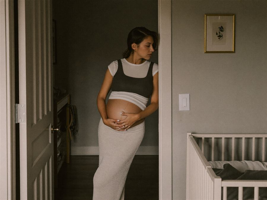 A pregnant woman resting her hand on her belly by the nursery crib